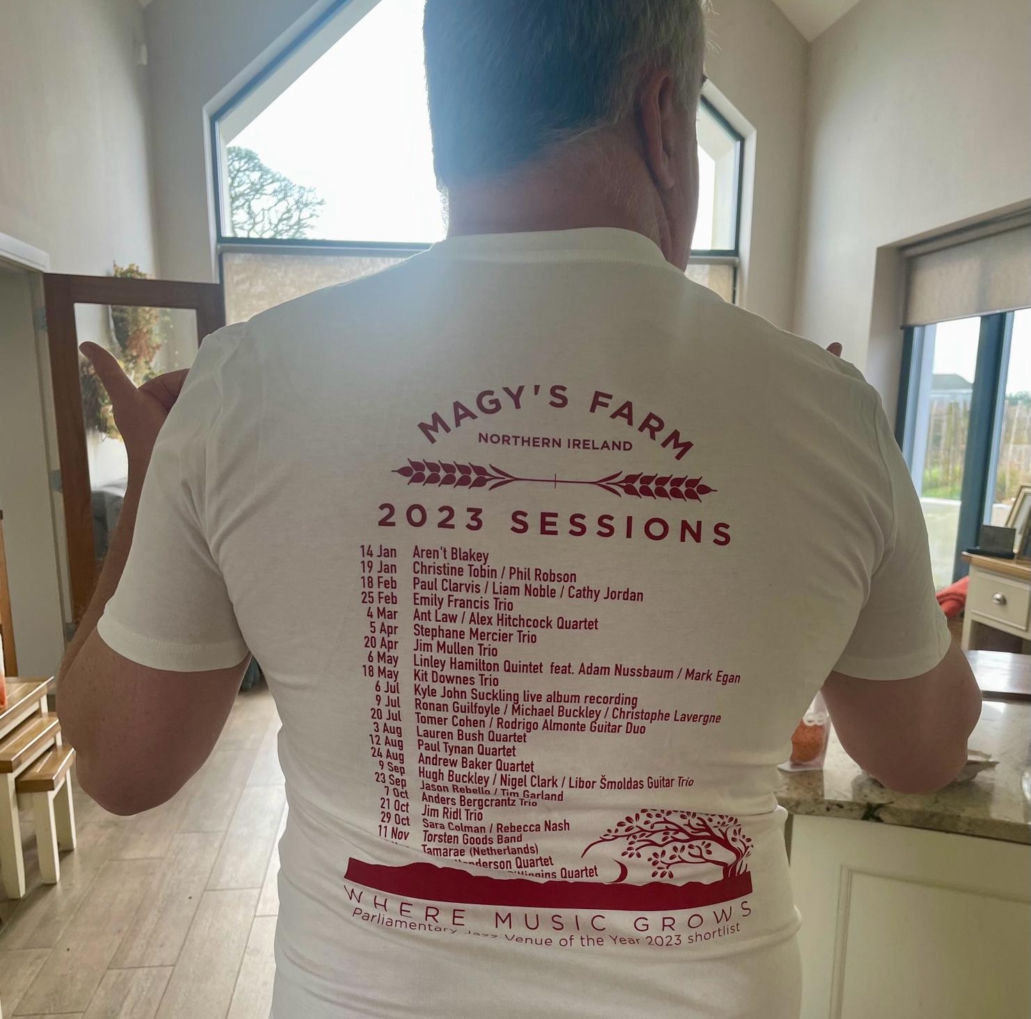 Linley Hamilton wears Magy's Farm merchandise, a white tshirt with red writing listing the session dates of jazz performances at the venue